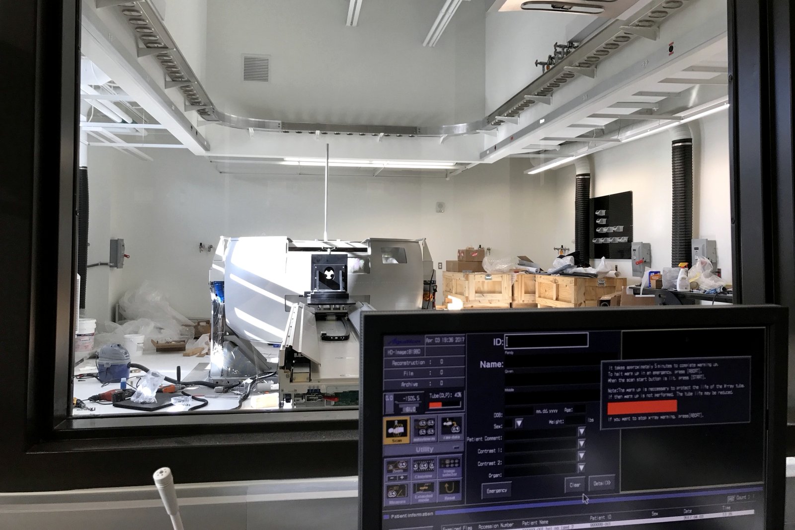View from the control room into the scanner room during the conversion: the CT gantry with covers off, shipping crates, the console in the foreground